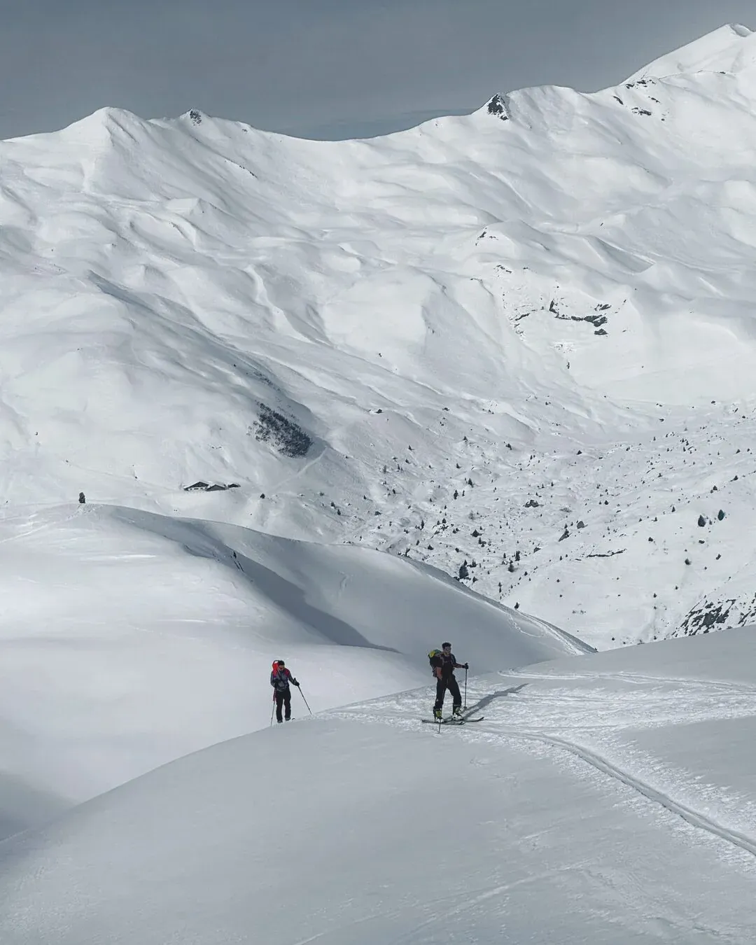 Two ski tourers on a snowy ridge below a sunlit mountain crest